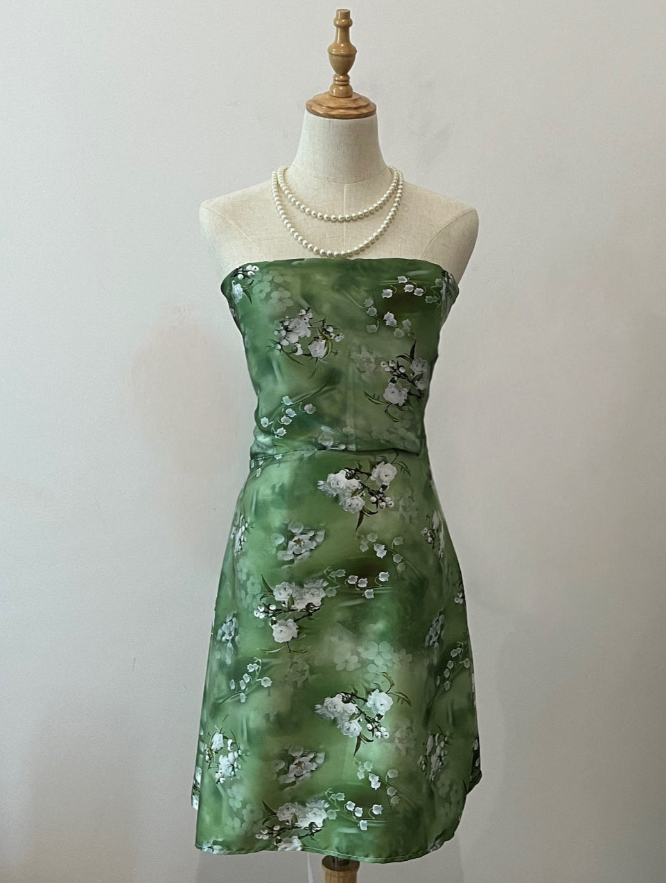 A mini silk corseted dress displayed on a mannequin, featuring a green floral pattern.